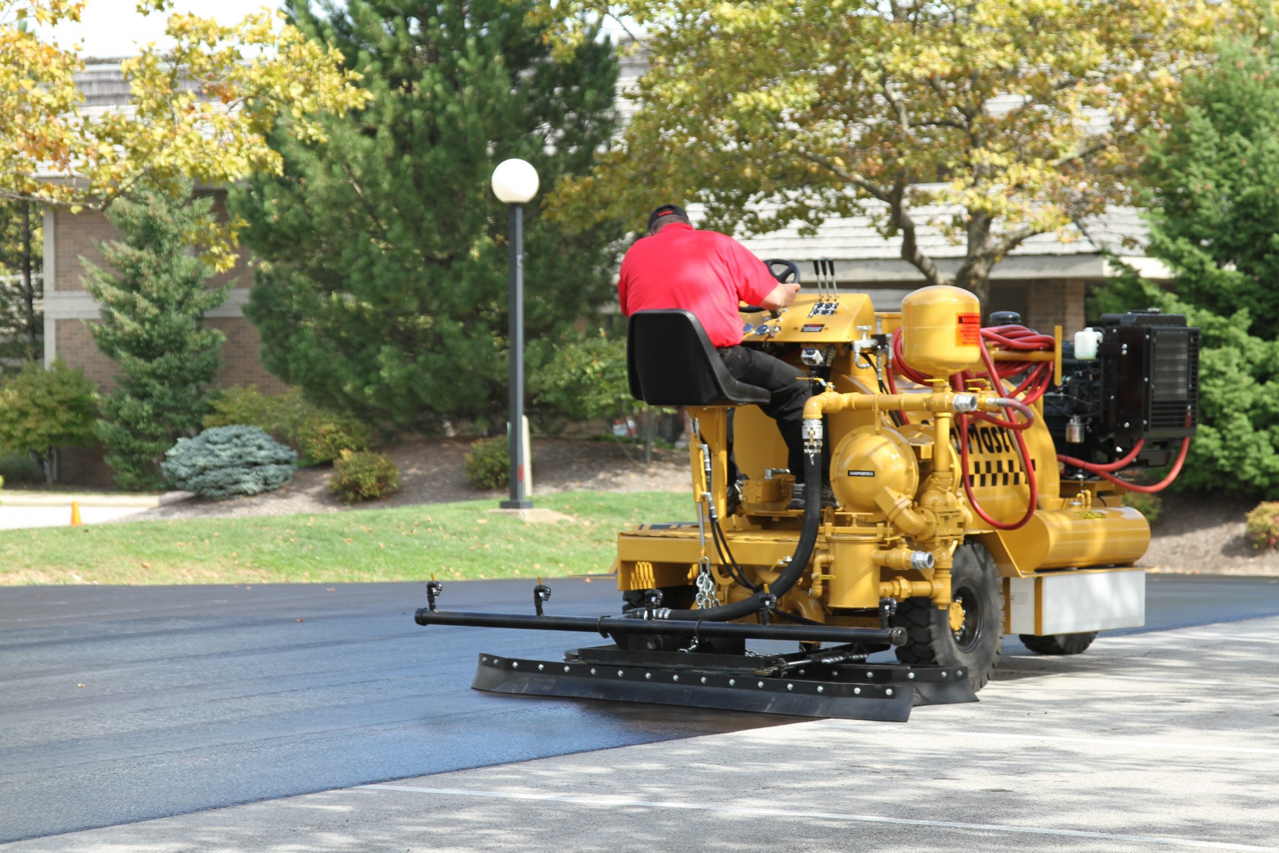 Squeegeeing asphalt-based sealer onto a business parking lot using a SealMaster SP 300 Dual Spray & Squeegee Machine.