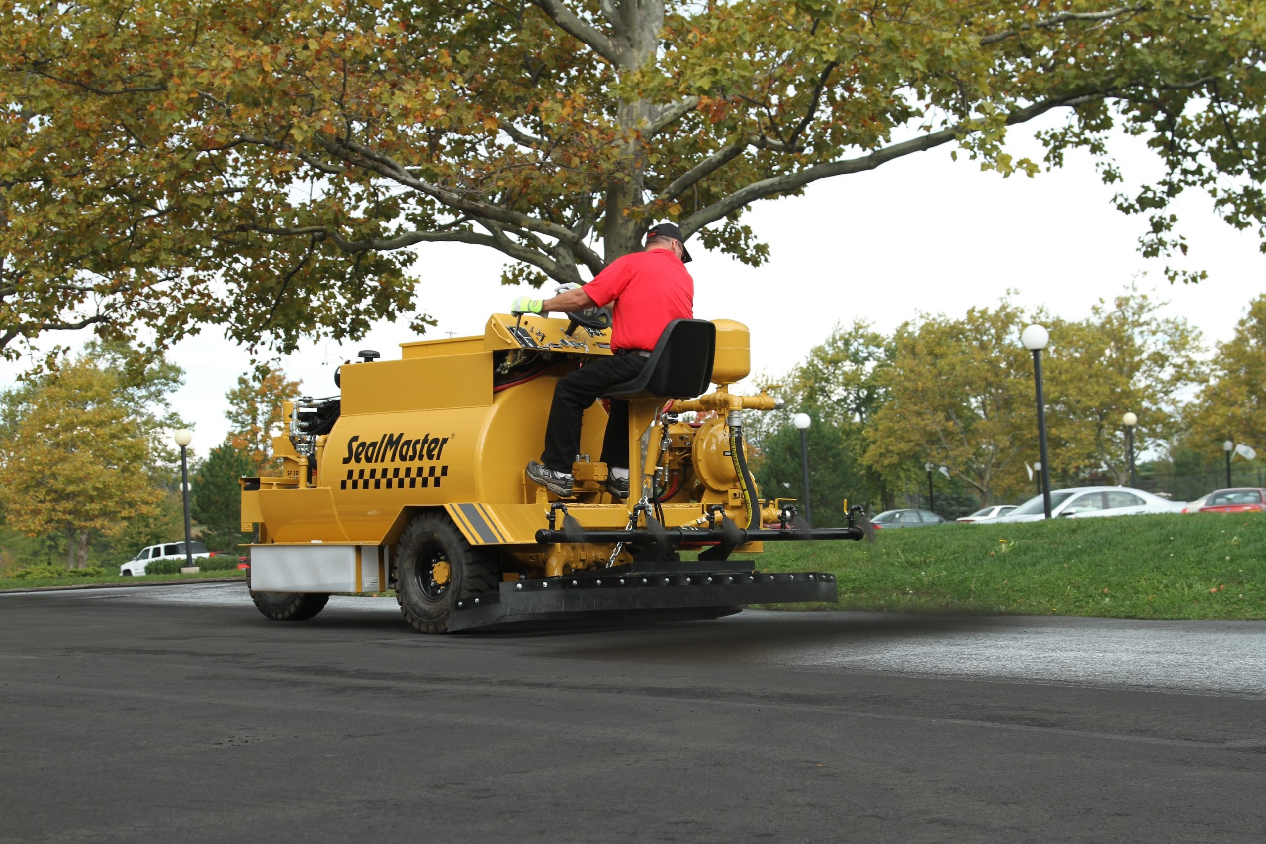 Spraying asphalt-based sealer onto a business parking lot using a SealMaster SP 300 Dual Spray & Squeegee Machine.